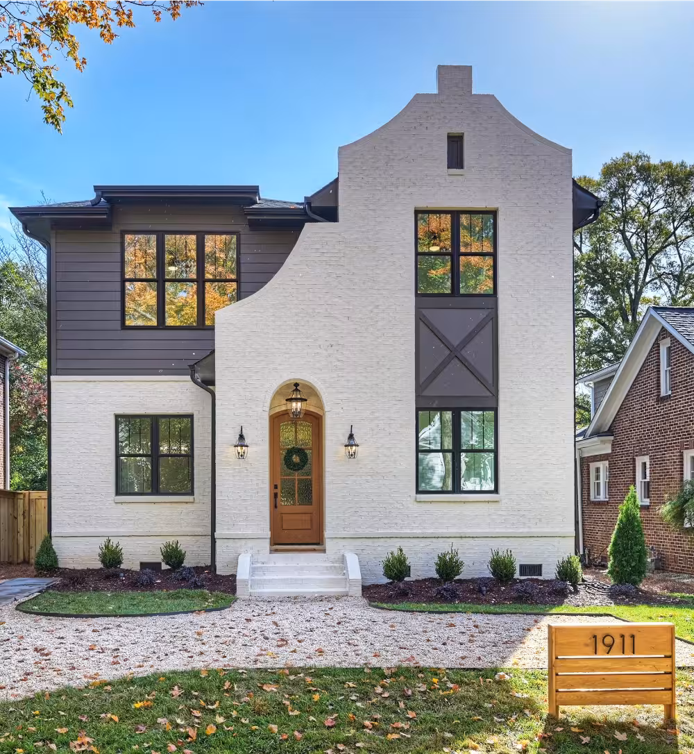 Two-story modern house with white brick exterior, dark trim, large windows, wooden front door, small front yard, and a sign displaying the number 1911.