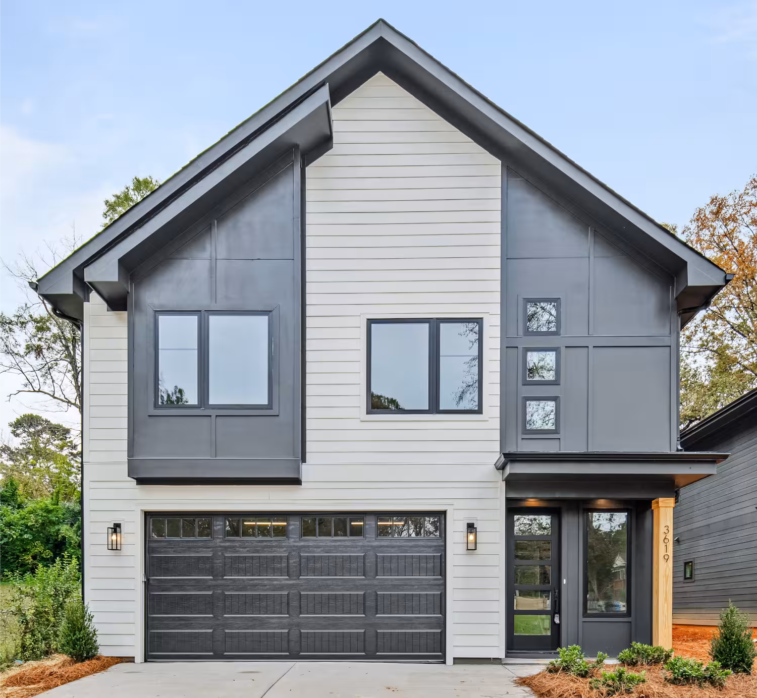 Two-story modern house with a gray and white exterior, large windows, a black double garage door, and small front lawn.